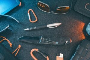 Une présentation à plat des articles essentiels du quotidien, notamment un couteau, un stylo, des lunettes de soleil et un mousqueton.