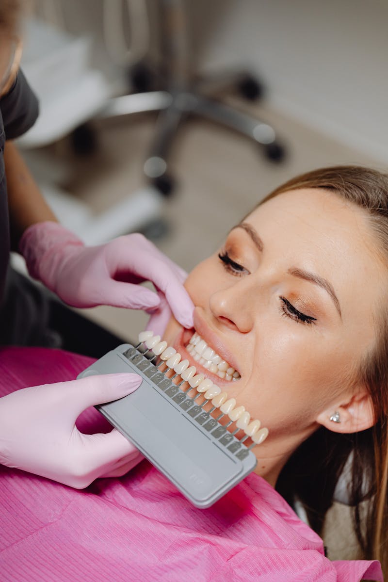 Une femme subissant un contrôle dentaire avec un nuancier pour faire correspondre la couleur des dents dans une clinique dentaire.